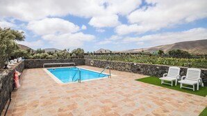 A swimming pool with a stone deck, two white lounge chairs, and a stone wall with plants.