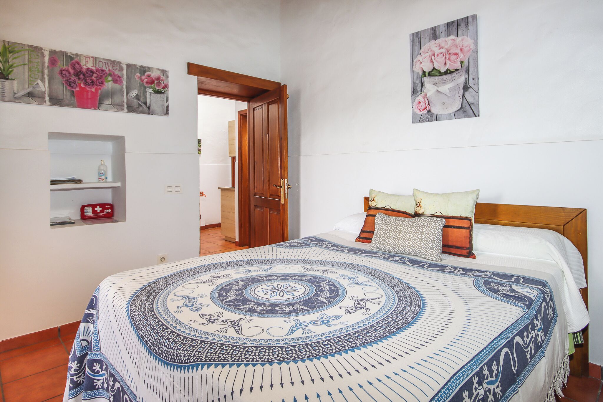 A bedroom with a bed, a door, a wall shelf, and a painting.