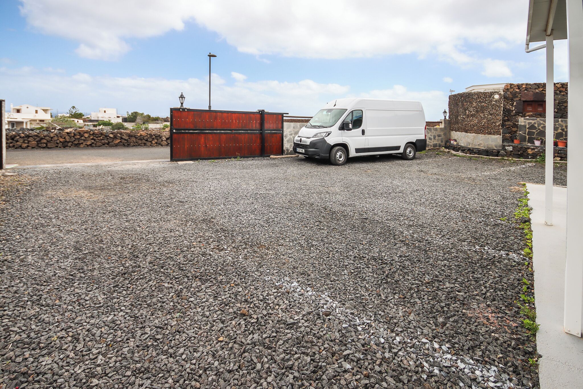 A gravel parking area with a white van parked near a red gate.