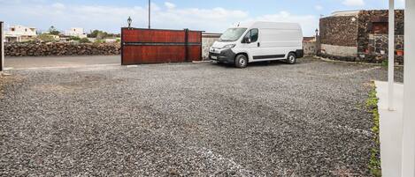 A gravel parking area with a white van parked near a red gate.