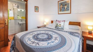A bedroom with a bed, a nightstand, a bedside lamp, a painting on the wall, and a bathroom with a mirror and sink.