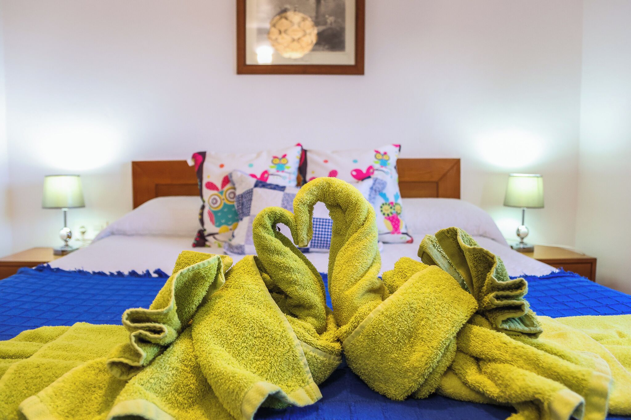 Ein Bett mit blauer Bettdecke, zwei Kissen mit bunten Mustern und zwei Nachttischlampen.