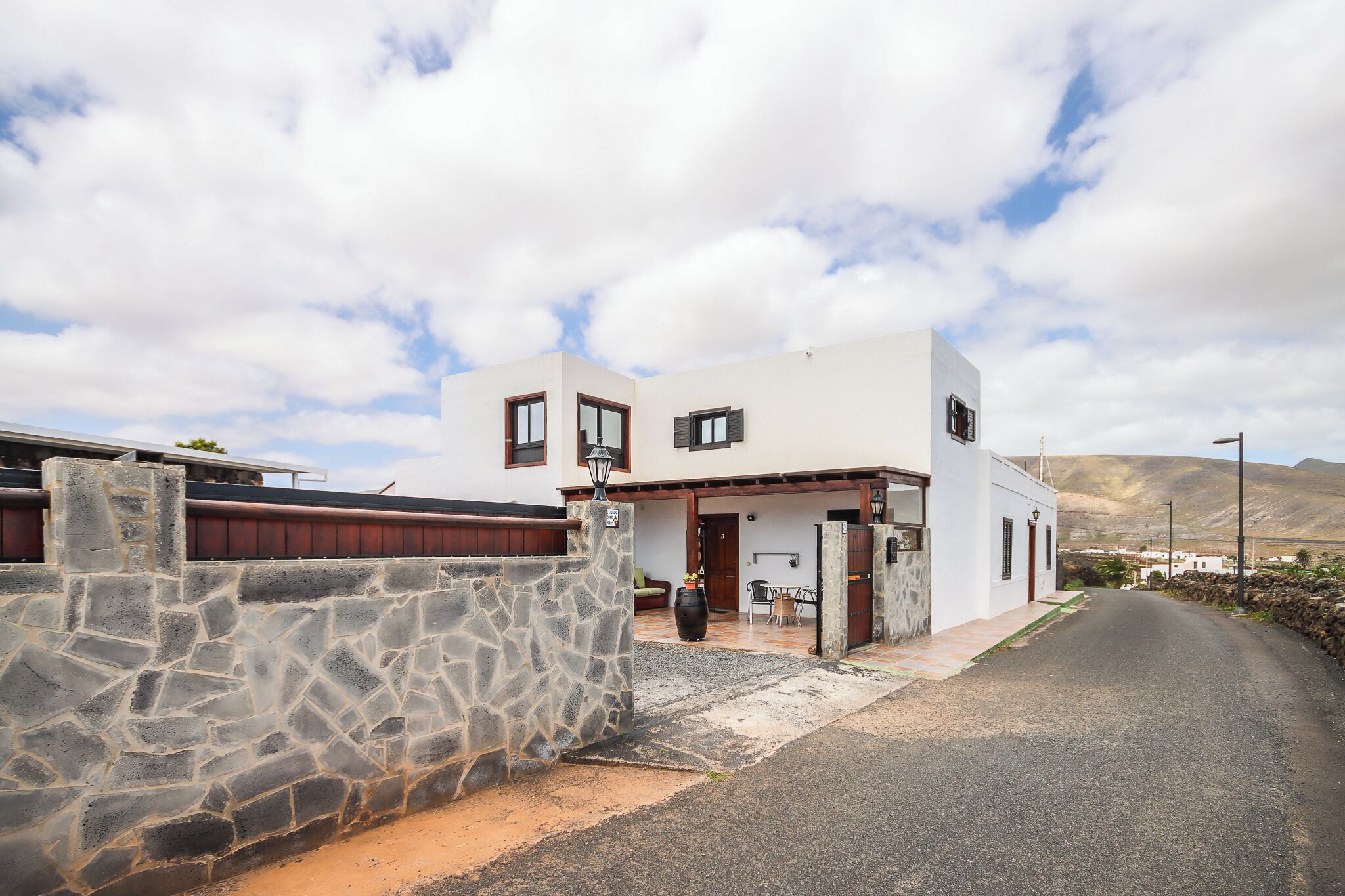 A two-story house with a stone wall entrance, a patio, and a mountainous backdrop.