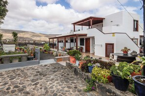 A white building with a covered patio, potted plants, and a stone-paved area. - Finca Villanueva (Mala)