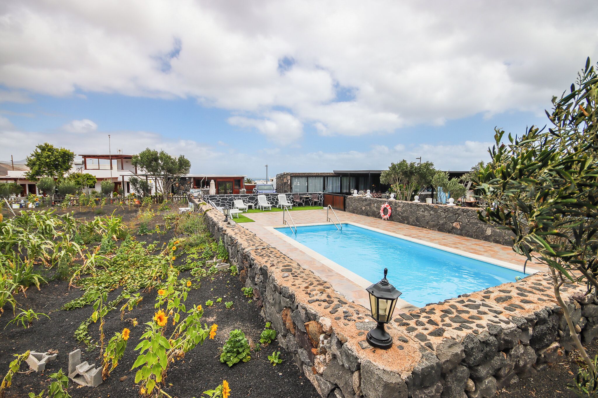 Una piscina circondata da un muro in pietra, con un giardino e un'area salotto all'aperto.
