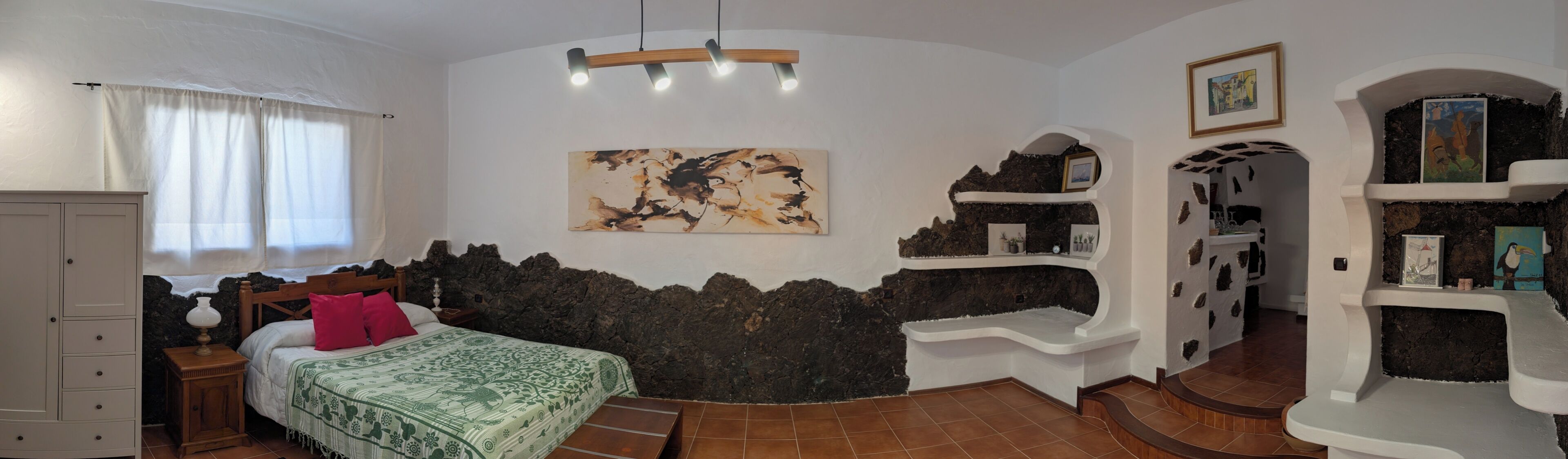 A bedroom with a bed, a nightstand, a dresser, a painting, and a unique stone wall design.