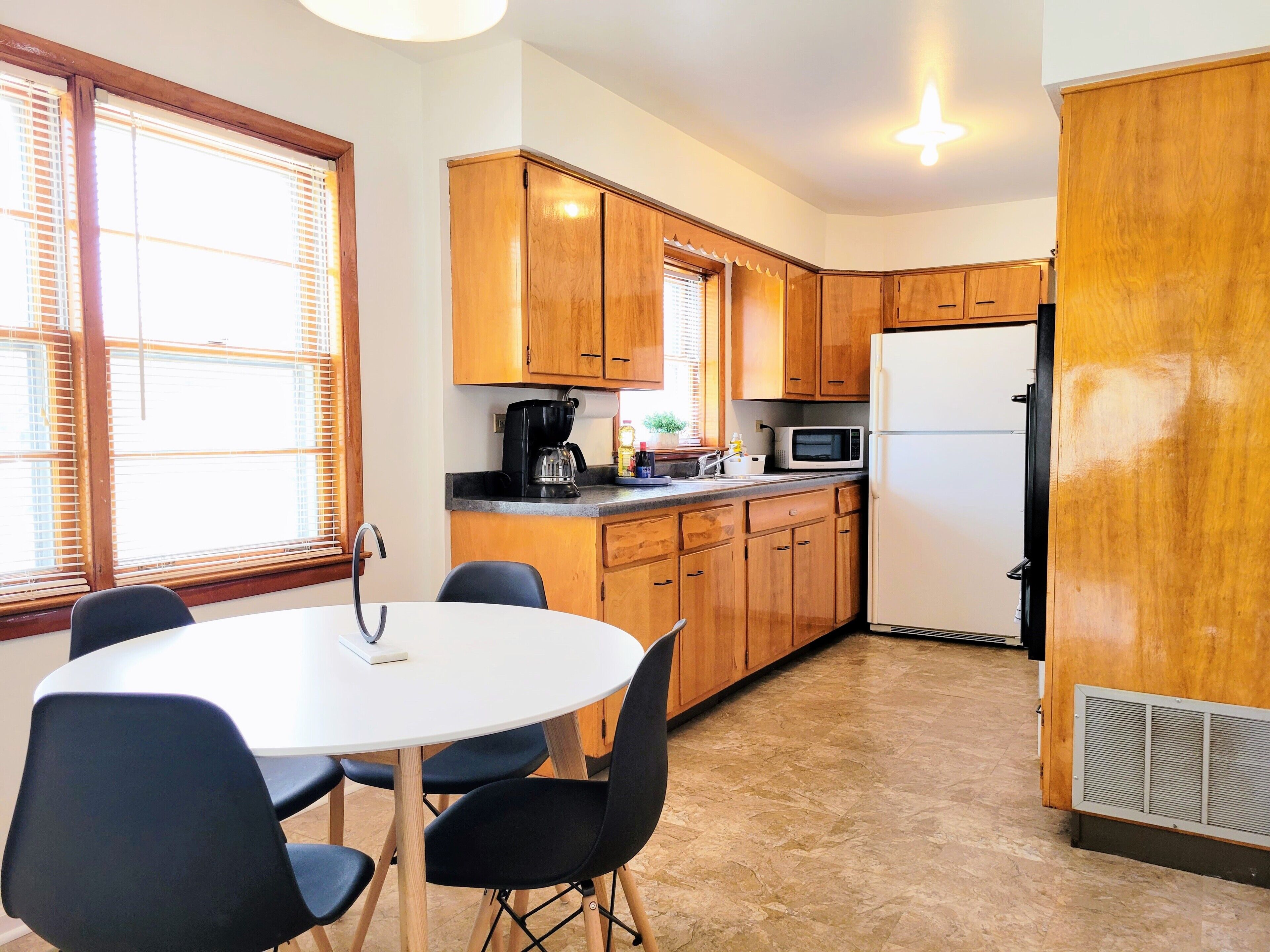 A compact kitchen with wooden cabinets, a white refrigerator, a microwave, and a coffee maker. There is a round table with four chairs.