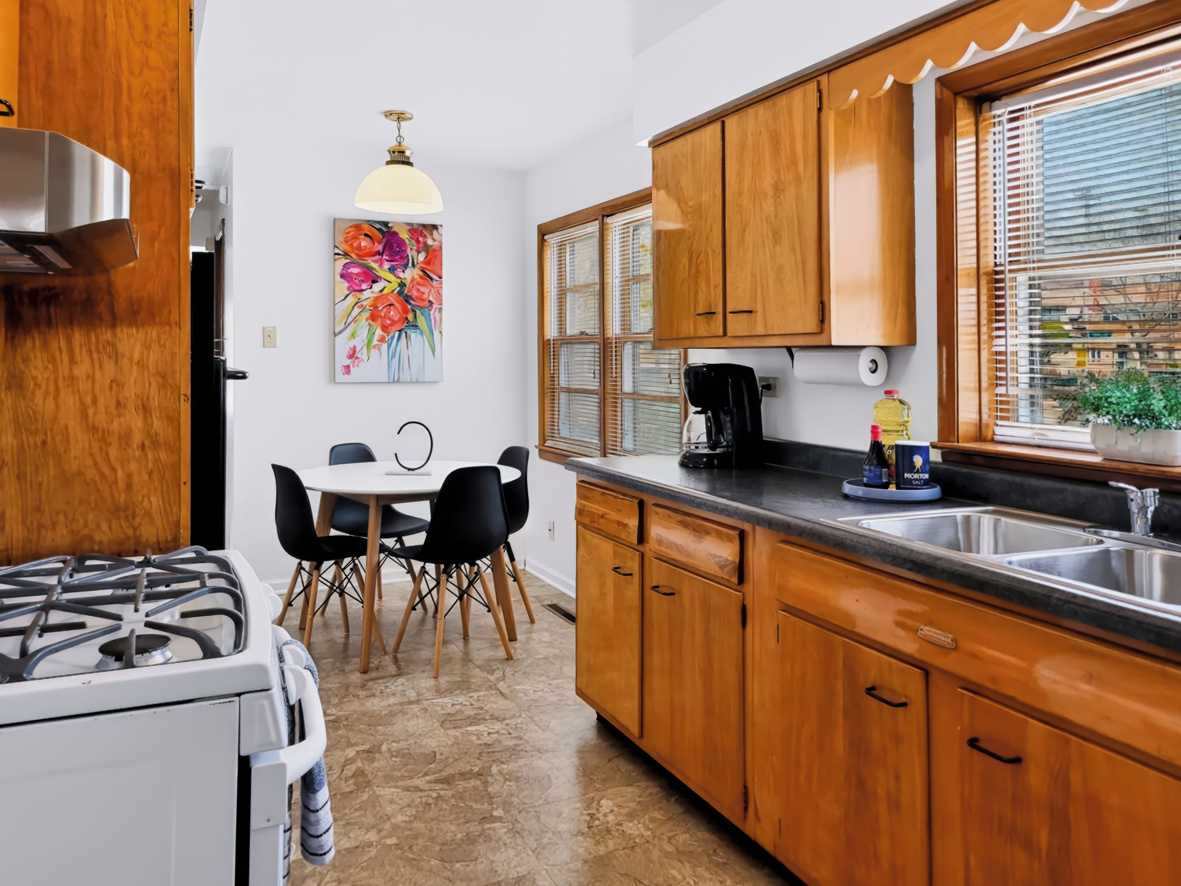 Een moderne keuken met houten kastjes, een gasfornuis, een eettafel met stoelen en een koffiezetapparaat.