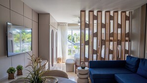 Un salon moderne avec un canapé, un téléviseur fixé au mur, un coin repas avec une table et une vue par la fenêtre.