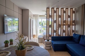 Un salon moderne avec un canapé, un téléviseur fixé au mur, un coin repas avec une table et une vue par la fenêtre.