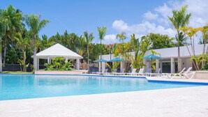 Une piscine entourée de palmiers et agrémentée d’un kiosque, avec des chaises longues et des parasols à proximité.