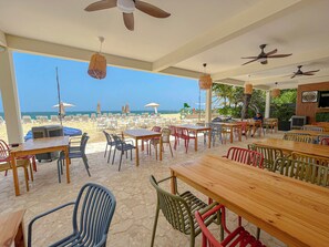 Un espace de restauration en plein air, avec des tables et des chaises, donnant sur une plage.