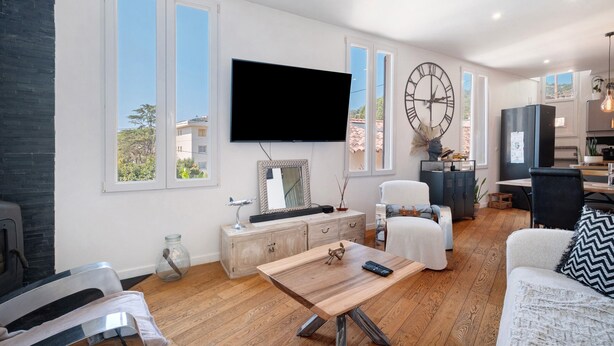 Ein modernes Wohnzimmer mit Flachbildfernseher, Couch, Holztisch und einem Essbereich. Im Hintergrund ist eine Küche zu sehen.