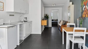 Une cuisine moderne avec des meubles blancs, un coin repas doté d’une table en bois et de chaises blanches, et un salon avec un canapé.