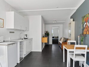 Eine moderne Küche mit weißen Schränken, ein Essbereich mit einem Holztisch und weißen Stühlen sowie ein Wohnzimmer mit einer Couch.
