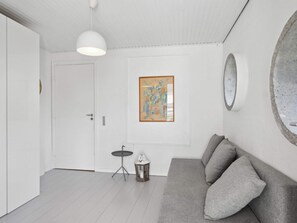 A room with a grey sofa, a white door, a small round mirror, and a framed abstract painting on the wall. - 5 Star Holiday Home in Koge (Koge)