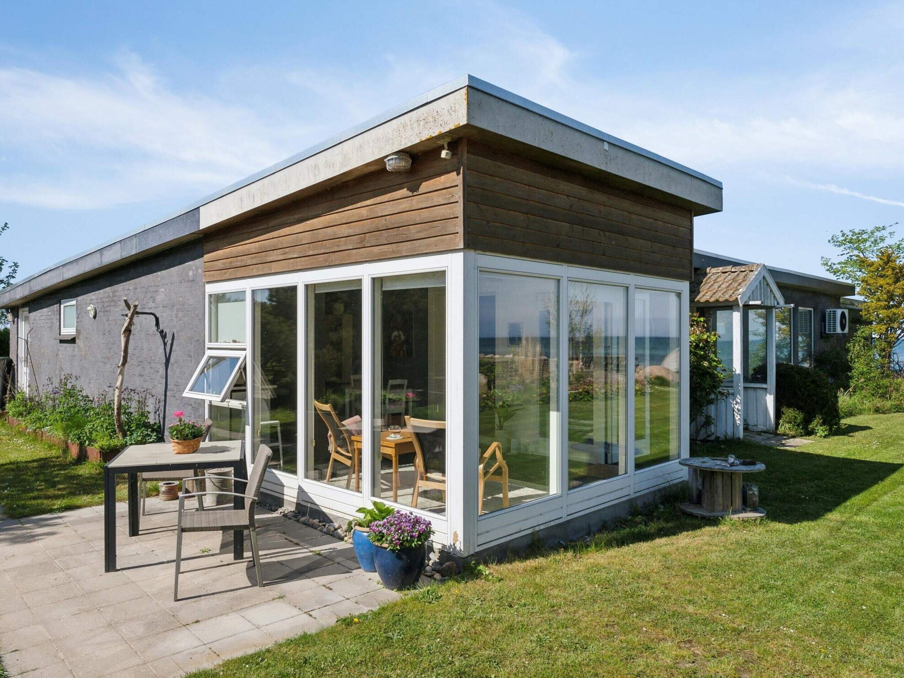 A modern house with a glass-enclosed patio, a wooden deck, and a garden.