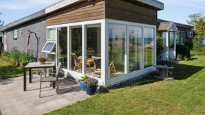 Une maison moderne dotée d’un patio entièrement vitré, d’une terrasse en bois et d’un jardin.