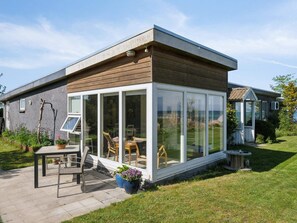 Ein modernes Haus mit einer gläsernen Veranda, einer Holzterrasse und einem Garten.