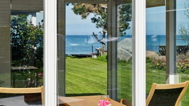 Une porte vitrée donne accès à une terrasse aménagée avec une table, des chaises et une vue sur la mer.