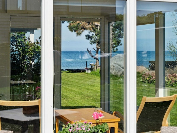 Eine Glastür führt zu einer Terrasse mit Tisch, Stühlen und Blick auf das Meer.