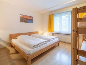 A double bed with wooden headboard, a bedside table, a lamp, and a window with curtains. - Val Signina 3-5 by Interhome (Laax)