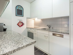 A kitchen with white cabinets, a granite countertop, a stainless steel sink, and a dishwasher. - Val Signina 3-5 by Interhome (Laax)
