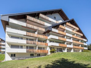 A multi-story building with balconies, a sloped roof, and a grassy hillside. - Val Signina 3-5 by Interhome (Laax)