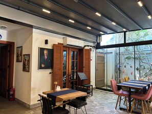 A restaurant with a wooden table and chairs, a fire extinguisher, and a large window with a view of trees.