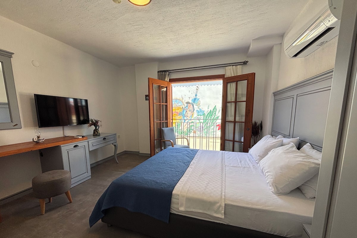 Ein Schlafzimmer mit Bett, Schreibtisch, Stuhl, Fernseher und einem Balkon mit Aussicht.