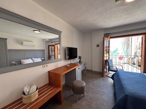 Habitación de hotel con un espejo grande, un escritorio de madera, televisión, balcón con una silla y una cama.
