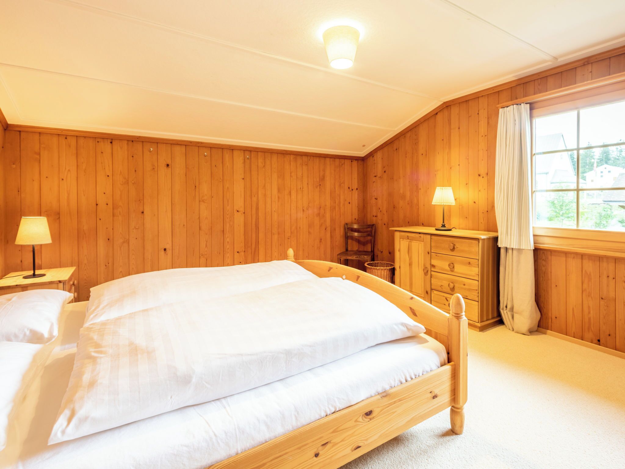 A wooden-paneled bedroom with a bed, nightstands, a dresser, and a window.