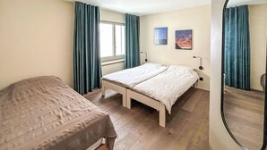 Une chambre avec deux lits, une fenêtre avec des rideaux, un miroir fixé au mur et deux tableaux encadrés.