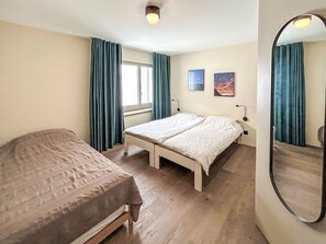 Ein Schlafzimmer mit zwei Betten, einem Vorhangfenster, einem Wandspiegel und zwei gerahmten Bildern.