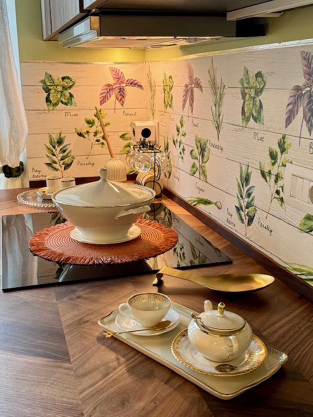 Una cucina con un set da tè su un vassoio, una ciotola su un piedistallo e una parete decorata con illustrazioni botaniche.