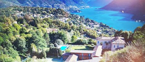 A mountainous landscape with a body of water, houses, and a swimming pool.