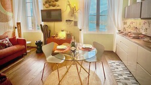 Ein Wohnzimmer mit Glastisch, einer Couch, einem Fernseher und einer Küchenzeile mit Fenster.