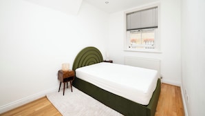 Quarto com uma cama, mesa de cabeceira, cadeira, janela e radiador.