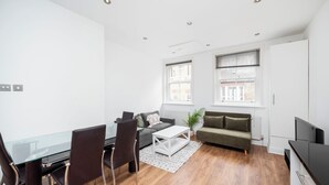 Um apartamento moderno com área de jantar, dois sofás, uma mesa de centro e uma televisão.