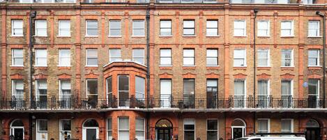 A row of red brick townhouses with white-framed windows, a black car parked in front, and a white van with a logo on the side.