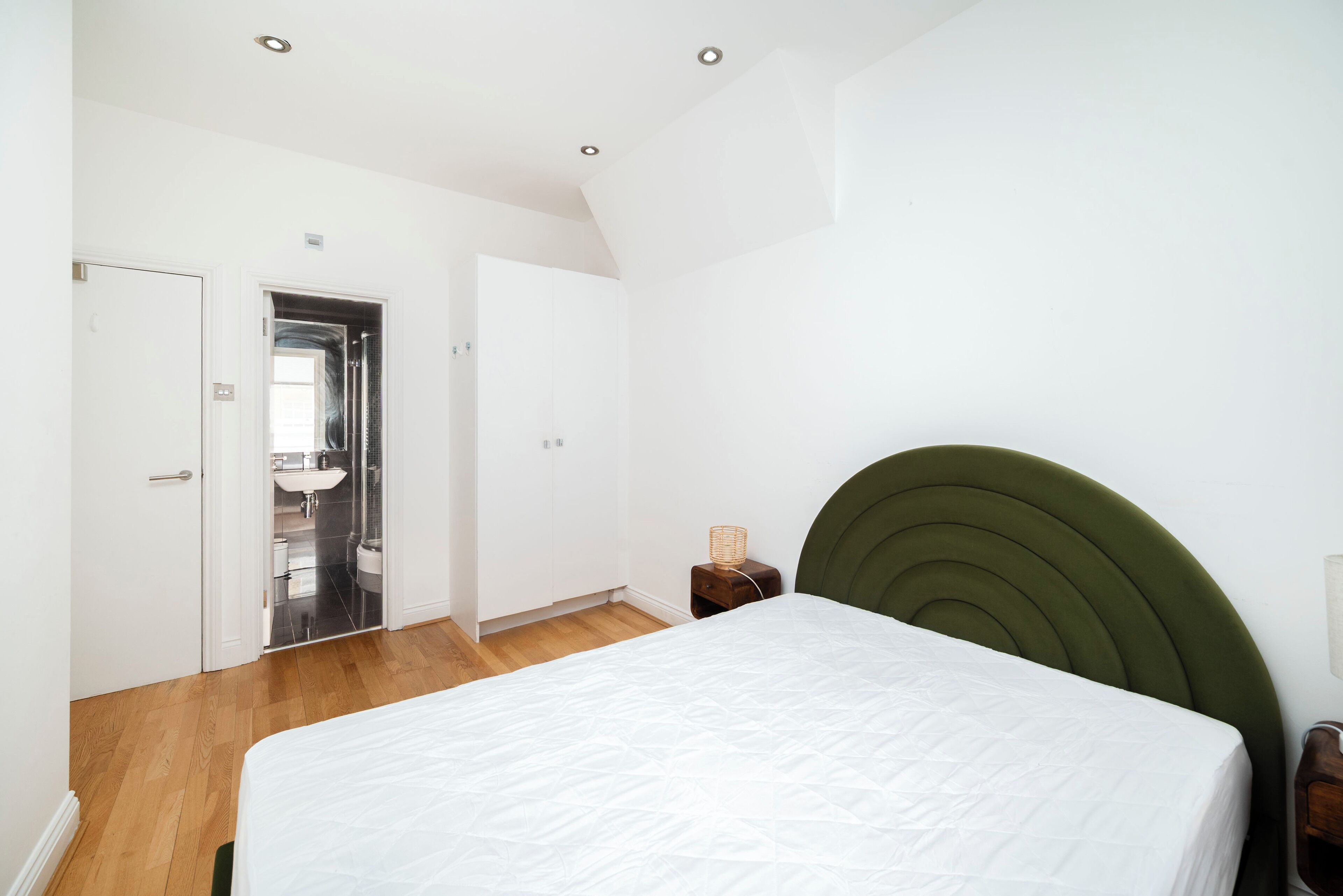 A bedroom with a bed, a wooden nightstand, a green headboard, and a white door leading to a bathroom.