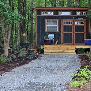 Eine Holzhütte mit einer Holzterrasse, einer kleinen Veranda und einem Kiesweg, der zum Eingang führt.