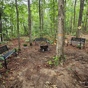 A forested area with benches and a fire pit.