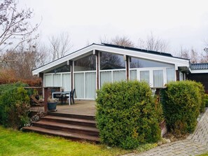 Ein modernes Haus mit überdachter Veranda, einem Essbereich mit Gartenmöbeln und einem gepflegten Garten.
