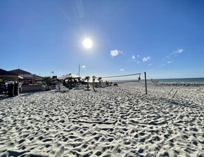 Ein Sandstrand mit Volleyballnetz, Sonnenschirmen und einem Gebäude mit einem Schild.