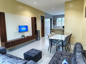 Ein modernes Wohnzimmer mit Flachbildfernseher, einem Essbereich mit Tisch und Stühlen und einer Küche im Hintergrund.