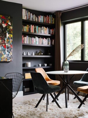 Ein modernes Interieur mit Bücherregal, Esstisch und Stühlen sowie einem großen Fenster.
