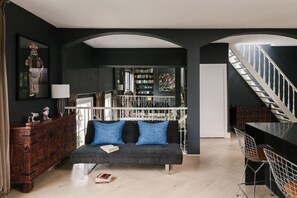 Una sala de estar moderna con una paleta de colores oscuros, un sofá con cojines azules, un aparador de madera, una escalera y una estantería.