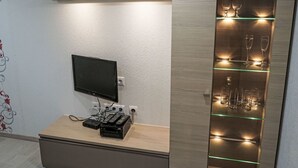 A modern room with a flat-screen TV mounted on the wall, a wooden entertainment unit with electronic devices, and a glass display case with wine glasses. - Apartment Jessy by Interhome (Gau-Algesheim)