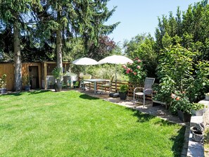 Ein Garten mit Rasenfläche, Holzzaun, einem Tisch mit Stühlen und Kübelpflanzen.